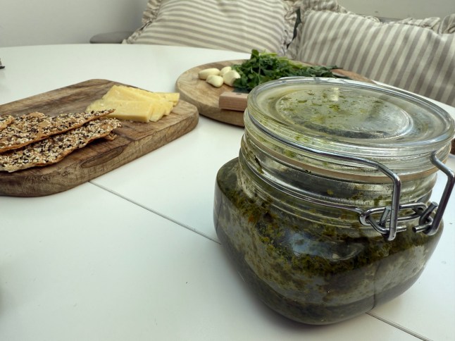 A jar of Sam's homemade chimichurri with cheese and crackers on a table