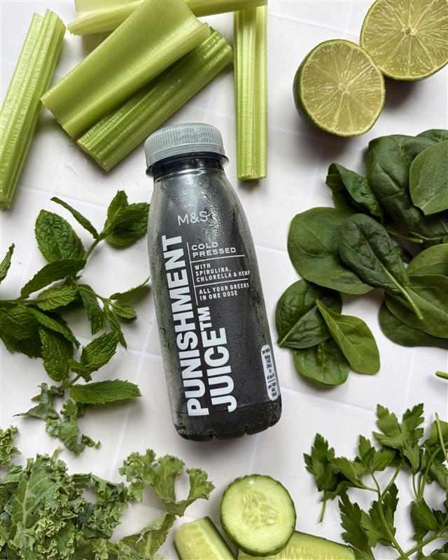 A bottle of M&S Punishment Juice, with veggies and herbs around it