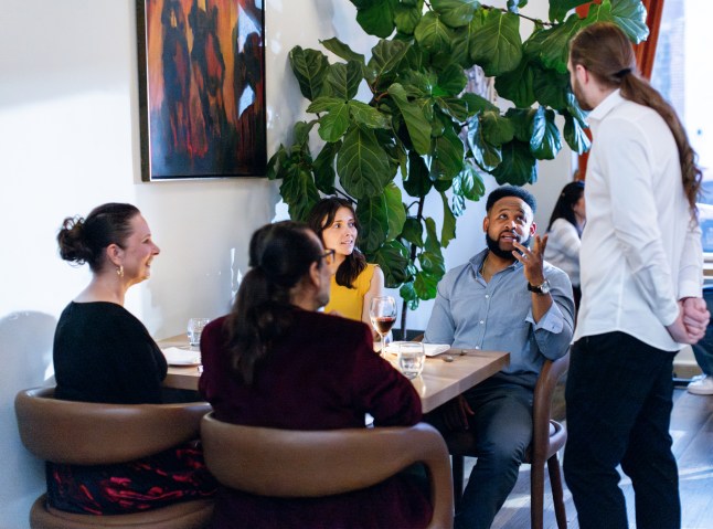 A waiter speaks with a table of four diners at an upscale restaurant
